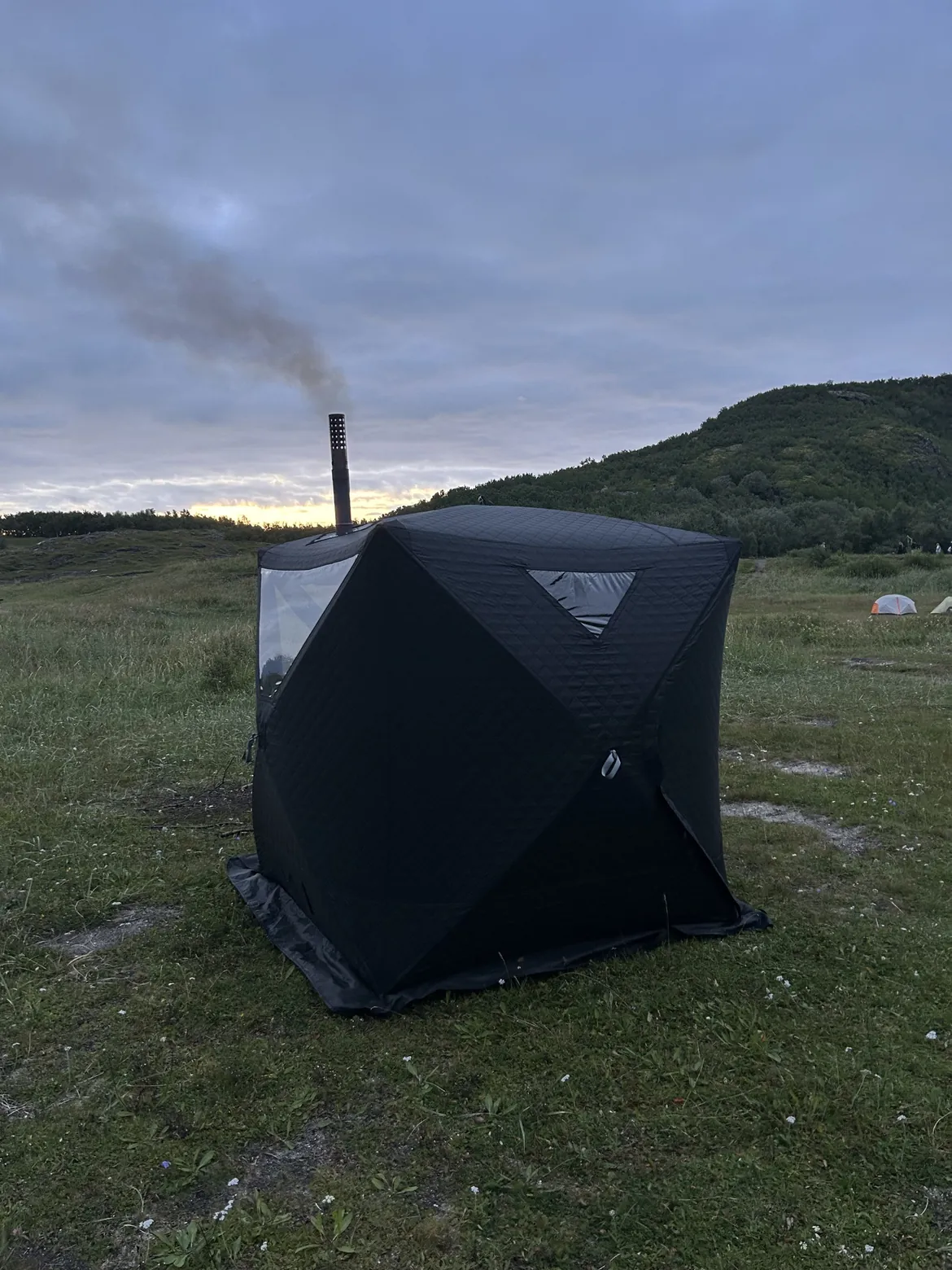 Badstutelt med røyk fra pipa på en gresslette en sommerkveld – leie badstue i Bodø