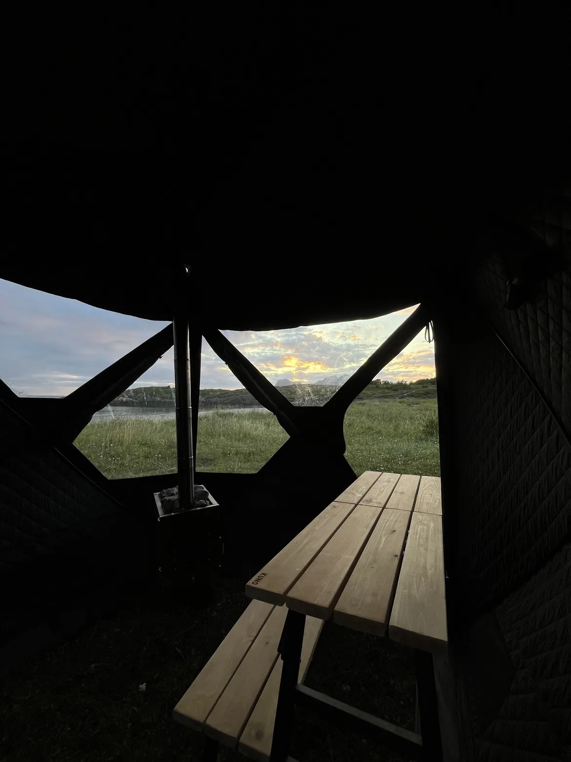 Benker og vedovn inne i badstuteltet med utsikt gjennom panoramavinduene – leie badstue i Bodø