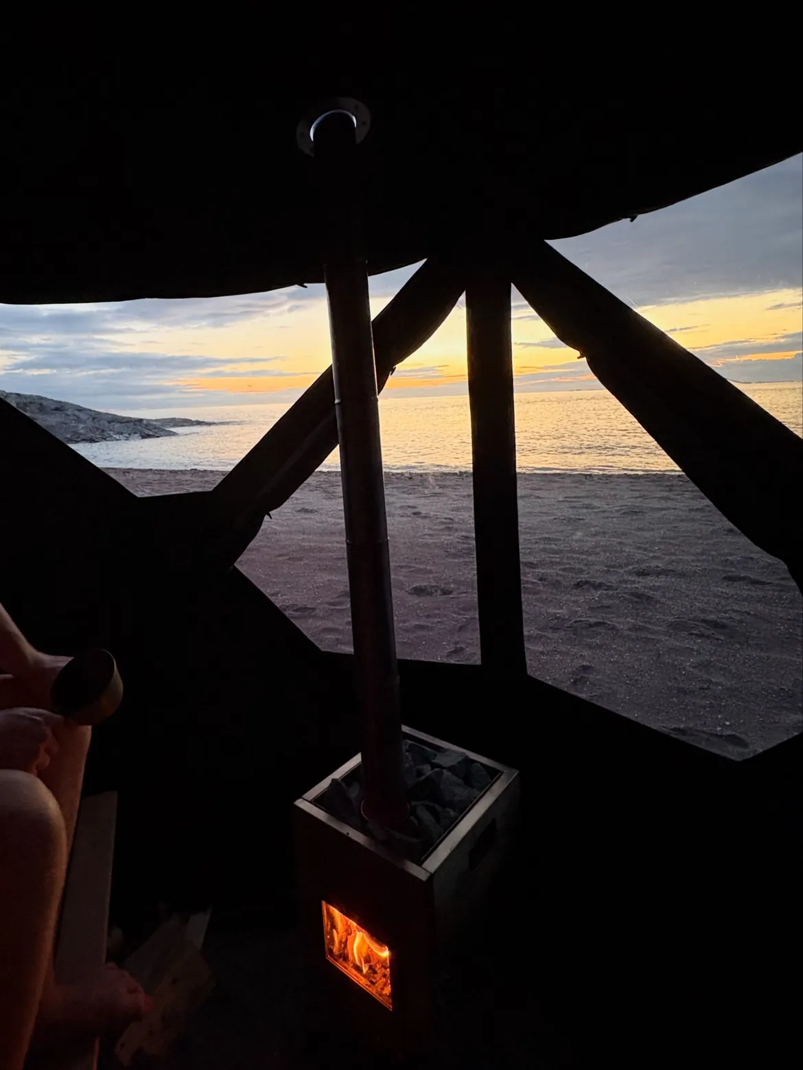 Innvendig i badstuteltet med fyr i vedovnen og solnedgang over havet – leie badstue i Trondheim